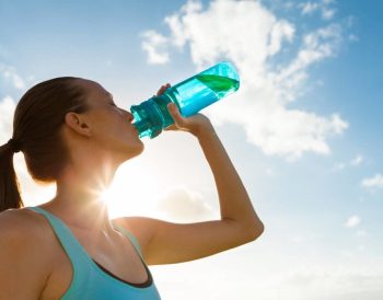 Bir cam sürahi ve limon dilimli su dolu bardak, yanında taze nane yapraklarıyla doğal bir ortamda sergileniyor.
