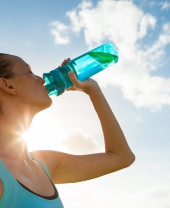 Bir cam sürahi ve limon dilimli su dolu bardak, yanında taze nane yapraklarıyla doğal bir ortamda sergileniyor.