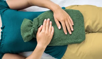 Sıcak su torbası tutan genç kadın, menstrual dönemde rahatlama arıyor.