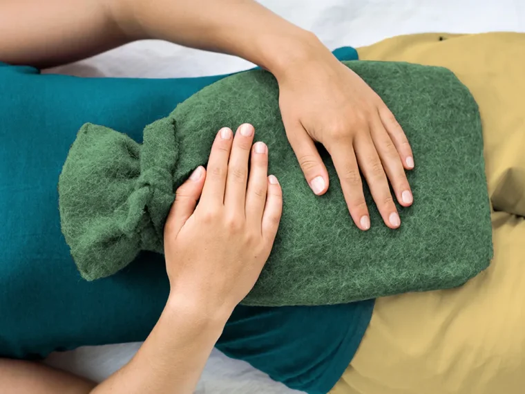 Sıcak su torbası tutan genç kadın, menstrual dönemde rahatlama arıyor.
