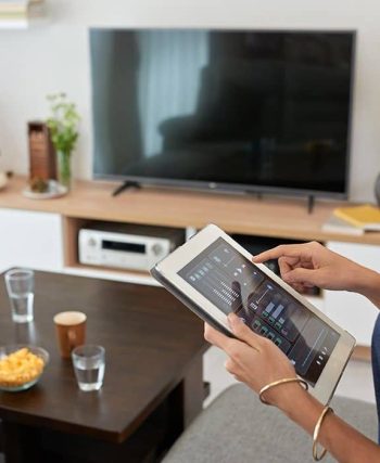 Oturma odasında akıllı aydınlatma, güvenlik kamerası, termostat ve sesli asistan gibi cihazların kullanıldığı modern bir ev ortamı.