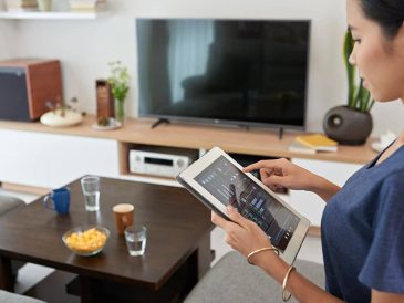 Oturma odasında akıllı aydınlatma, güvenlik kamerası, termostat ve sesli asistan gibi cihazların kullanıldığı modern bir ev ortamı.