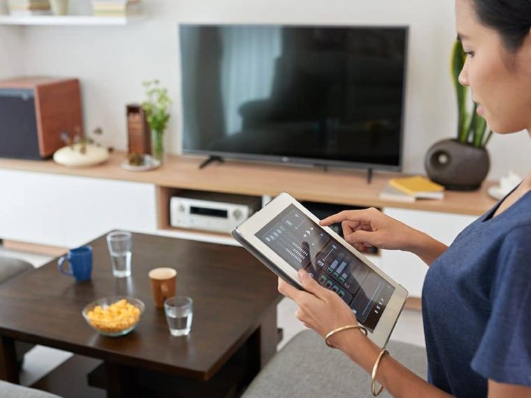 Oturma odasında akıllı aydınlatma, güvenlik kamerası, termostat ve sesli asistan gibi cihazların kullanıldığı modern bir ev ortamı.