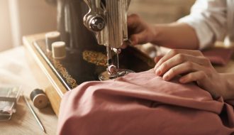 Dikiş makinesi kullanmadan, iğne ve iplik ile basit bir elbise hazırlama sürecini gösteren çalışma masası ve malzemeler.