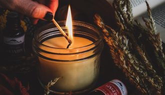 Cam kavanozlarda hazırlanmış, üzeri kuru portakal dilimleri, tarçın çubukları ve lavanta taneleriyle süslenmiş ev yapımı doğal kokulu mumların ahşap bir sehpa üzerinde durduğu görüntü.