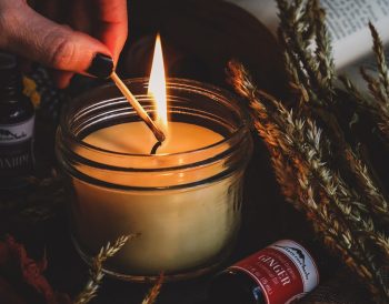 Cam kavanozlarda hazırlanmış, üzeri kuru portakal dilimleri, tarçın çubukları ve lavanta taneleriyle süslenmiş ev yapımı doğal kokulu mumların ahşap bir sehpa üzerinde durduğu görüntü.