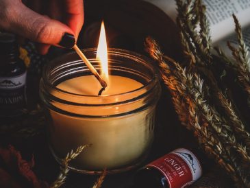 Cam kavanozlarda hazırlanmış, üzeri kuru portakal dilimleri, tarçın çubukları ve lavanta taneleriyle süslenmiş ev yapımı doğal kokulu mumların ahşap bir sehpa üzerinde durduğu görüntü.