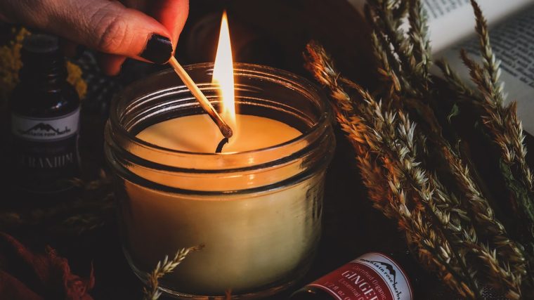 Cam kavanozlarda hazırlanmış, üzeri kuru portakal dilimleri, tarçın çubukları ve lavanta taneleriyle süslenmiş ev yapımı doğal kokulu mumların ahşap bir sehpa üzerinde durduğu görüntü.