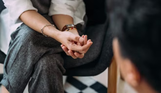 Bir çift el ele tutuşmuş, birbirlerine bakıyor; arka planda sakin bir ortam, güven ve yakınlık hissi yaratıyor.