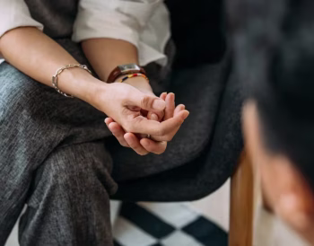 Bir çift el ele tutuşmuş, birbirlerine bakıyor; arka planda sakin bir ortam, güven ve yakınlık hissi yaratıyor.