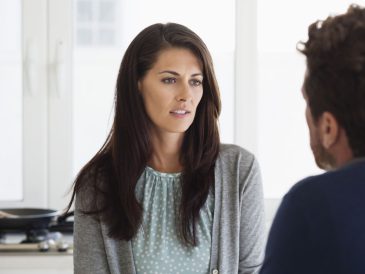Karşısındaki kişiye konuşurken tereddütle bakan, dudakları arasından “hayır” demeye çalışan bir kişinin düşünceli şekilde ellerini birleştirdiği anın görüldüğü, arka planı flu bir iç mekân sahnesi.
