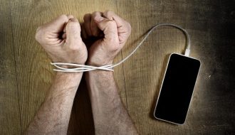 Bir kişi telefonunu bir kenara bırakıp kitap okuyor; yanında kahve ve not defteri var, telefon yerine farklı aktivitelerle vakit geçiriyor.