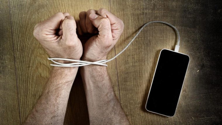 Bir kişi telefonunu bir kenara bırakıp kitap okuyor; yanında kahve ve not defteri var, telefon yerine farklı aktivitelerle vakit geçiriyor.