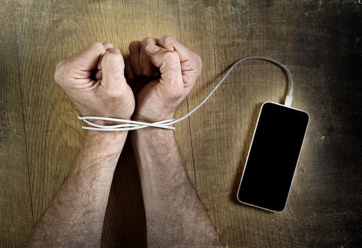 Bir kişi telefonunu bir kenara bırakıp kitap okuyor; yanında kahve ve not defteri var, telefon yerine farklı aktivitelerle vakit geçiriyor.