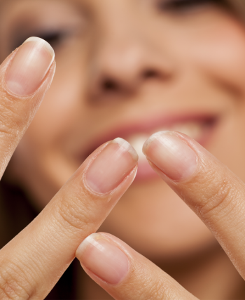 Badem, yumurta, avokado, yeşil yapraklı sebzeler ve su bardağının yer aldığı, sağlıklı tırnaklar için besleyici gıdaların bulunduğu ahşap masa düzeni.